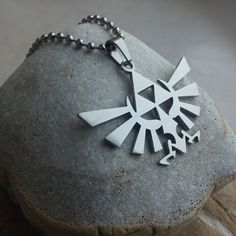 a silver necklace with an image of the legend of zelda on it sitting on top of a rock