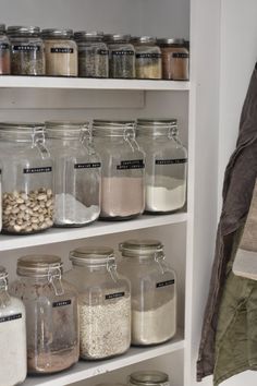 an organized pantry with glass jars and other items on the shelves, including beans, cereals, nuts, and more