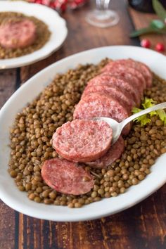 two white plates filled with meat and lentils on top of a wooden table next to wine glasses