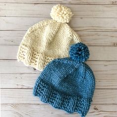 two knitted hats sitting on top of a wooden floor next to each other and one has a blue pom - pom