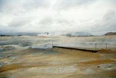 an open area with some water and steam coming out of the ground in the distance