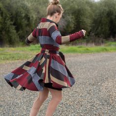 a woman in a dress is skateboarding on the gravel road with trees in the background