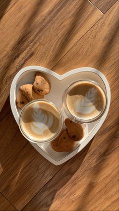 three cups of coffee with cookies in the shape of a heart on a wooden table