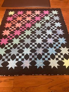 a black quilt with stars on it sitting on top of a wooden floor next to a table