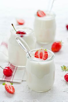 yogurt with strawberries in small glass jars on a white tablecloth and cherries