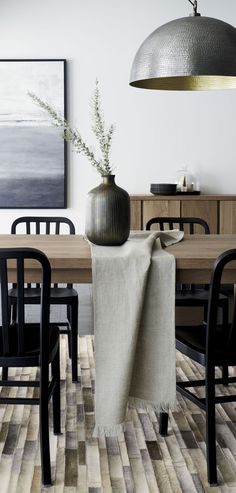 a dining room table with chairs and a vase on it's end, in front of a painting