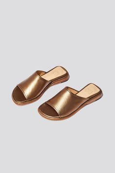 The Pileta slide is a streamlined version of the Pileta Sport Slide, featuring a sleek leather sole. The absence of details creates the perfect canvas for metallic bronze kidskin to shine. Slipping into a simple flat sandal in a striking material can be the answer to "dressing up" on a summer night when paired with a long strappy dress. Who it’s for: The woman who likes being the most comfortable person at the party.Kidskin upper with vegetable tanned leather lining and a 25 mm stacked leather h Gold Leather Sandals With Rubber Sole, Metallic Leather Mules For Summer, Gold Slides With Leather Footbed, Metallic Open Toe Mules For Summer, Gold Leather Footbed Slides, Metallic Open Toe Slides, Sleek Leather Slip-on Slides, Brown Leather-lined Slides For Summer, Brown Leather Sole Slides, Slip-on Fit