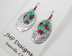 the earrings are decorated with red flowers and green leaves on silver disc shaped dangles