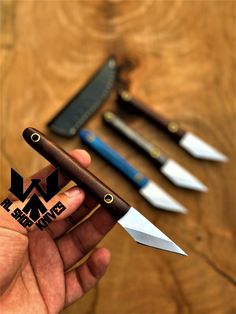 a person holding a knife and some knives on a wooden table in front of them