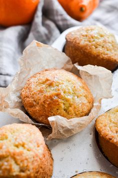 several muffins sitting on top of a white plate next to oranges and a gray towel