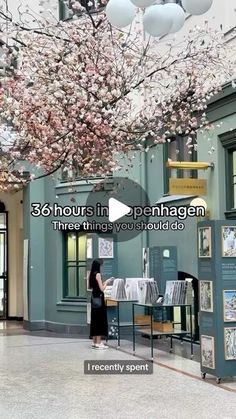 a woman standing under a tree filled with lots of pink flowers in a museum like setting