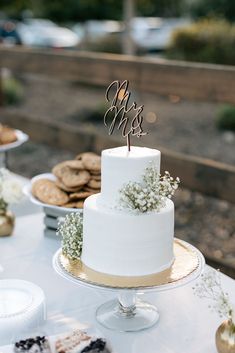 a white cake sitting on top of a table next to cookies and other desserts