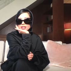 a woman sitting on top of a white couch wearing sunglasses and a black hoodie