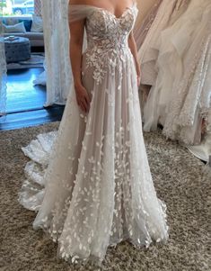 a woman standing in front of a mirror wearing a wedding dress with flowers on it