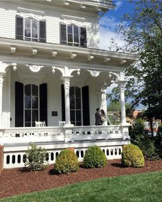 a white house with black shutters and two people standing on the porch in front