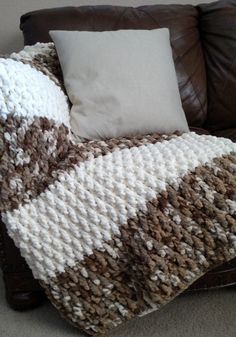 a couch with a blanket on top of it next to a brown leather chair and pillow