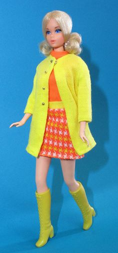 a barbie doll wearing a bright yellow coat and skirt with boots on her feet, standing in front of a blue background