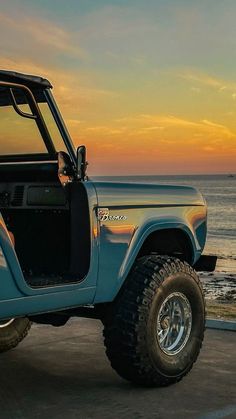 a blue jeep parked on the beach at sunset