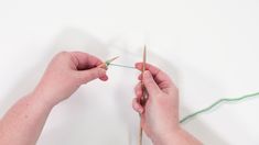 two hands holding yarn and knitting needles on a white surface