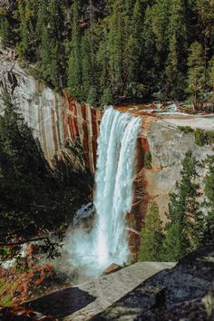 a waterfall with water cascading down it's sides and surrounded by trees