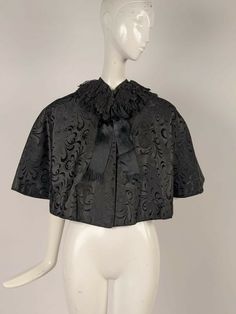 VICTORIAN 19TH C BLACK BROCADE SILK CAPE W CHANGEABLE LINING DATING TO THE VICTORIAN 19TH CENTURY FASHIONED OF A BLACK SILK RICH BROCADE WITH TWO ROWS OF BLACK CHANTILLY LACE RUFFLES ENCIRCLING THE NECKLINE.   SILK SATIN RIBBONS TRIM THE FRONT WITH A BOW AT THE NECKLINE AND THE INTERIOR IS IN A PURPLE AND GREEN CHANGEABLE SILK.   CONDITION:  THERE IS A SMALL FRAY AT THE CENTER REAR OF THE LINING AS WELL AS SOME FRAY AT THE CENTER REAR TOP NECKLINE IN THE LINING.   THE EXTERIOR HAS NO FLAWS, I WO Brocade Shirt, Silk Cape, Top Neckline, 19th Century Fashion, Satin Ribbons, Victorian Clothing, Chantilly Lace, Purple And Green, Lace Ruffle