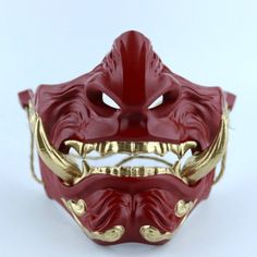 a red mask with gold details on the front and back sides, sitting on a white surface