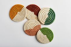 four woven coasters in different colors on a white surface with an orange, green, yellow and red design