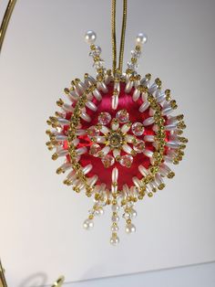 an ornament is hanging from a gold and red string with pearls on it