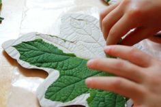 two hands are working on some green leaf shaped paper pieces with leaves scattered around them