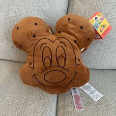 a brown mickey mouse pillow sitting on top of a couch next to a package of toys