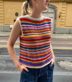 a woman standing in the street with her hands on her hips wearing a multicolored crocheted sweater