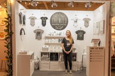 a woman standing in front of a booth with t - shirts on display