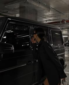 a woman walking towards a black vehicle in a parking garage with her hand on the door