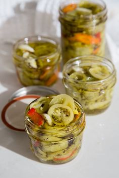 three jars filled with pickles and carrots sitting on a white table cloth next to each other