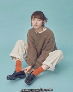 a woman sitting on the ground with her legs crossed wearing socks and a brown sweater