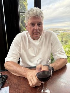 an older man sitting at a table with a glass of wine in front of him