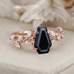 a black stone surrounded by white diamonds sits on top of a flowery cloth next to a ring