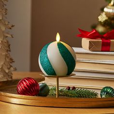 a candle that is sitting on a table next to some christmas ornaments and books with a tree in the background