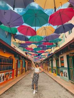 a woman is standing in the middle of an alley with many colorful umbrellas overhead