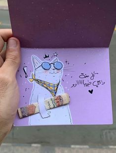 a person holding up a purple card with a cat wearing sunglasses and a scarf on it