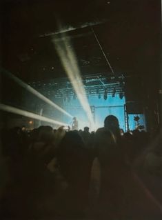 people are standing in front of a stage with bright beams coming from the ceiling and lights shining down on them