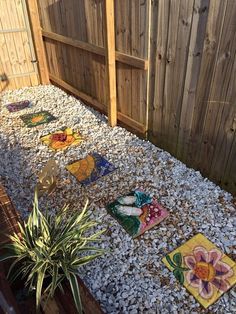 an outdoor area with gravel, rocks and flowers on the ground next to a wooden fence