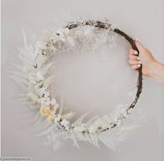 a hand holding a wreath made out of feathers and branches with white flowers on it