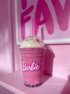 a pink drink sitting on top of a table next to a window with the word barbie written on it