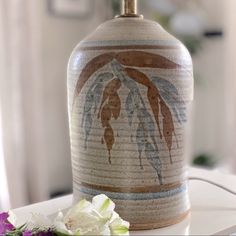 a vase sitting on top of a white table next to a purple and white flower