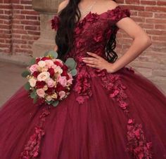 a woman in a red dress with flowers on her shoulder and long black hair standing next to a brick wall