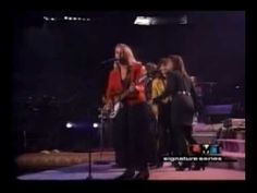 two women singing on stage with microphones in front of them and one woman holding a guitar