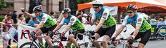 three bicyclists are riding down the street in front of a group of people