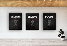 three black and white posters on the wall above a potted plant in an empty room