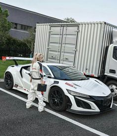 a woman standing next to a white sports car in front of a shipping container on the road